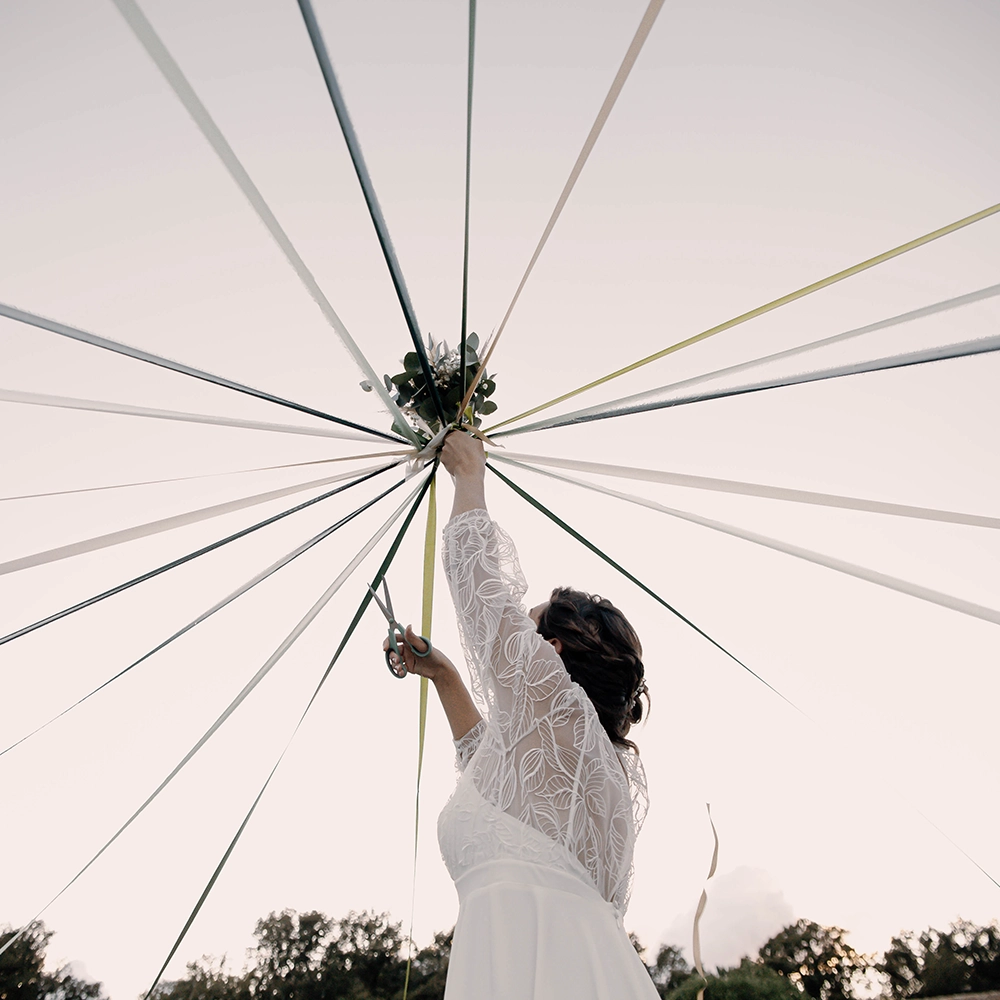 Mariée de dos en robe de dentelle, bras levés tenant un parasol graphique — shooting mariage artistique mari-on.fr
